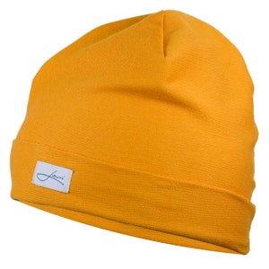 Puede incluir: Gorro de color amarillo mostaza con borde doblado. Una peque&ntilde;a etiqueta blanca con un logotipo azul est&aacute; cosida en la parte delantera. El gorro est&aacute; hecho de un tejido de punto suave.