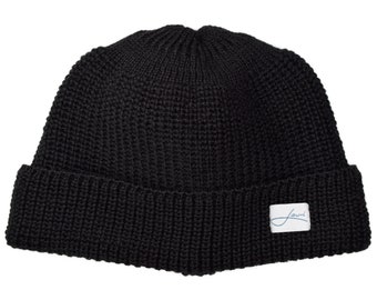 May include: A black knit beanie hat with a folded brim. The hat has a ribbed texture and a small white tag with a cursive logo. The beanie is a winter accessory.