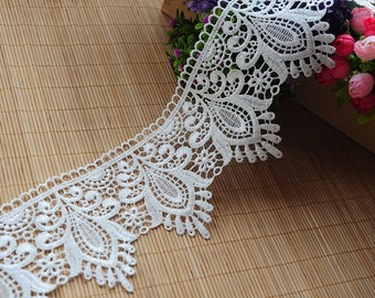 May include: White lace trim with a scalloped edge and a delicate floral pattern. The lace is approximately 2 inches wide.