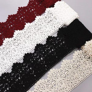 May include: Four different lace trims in white, black, cream, and burgundy. The lace has a delicate floral pattern with scalloped edges.