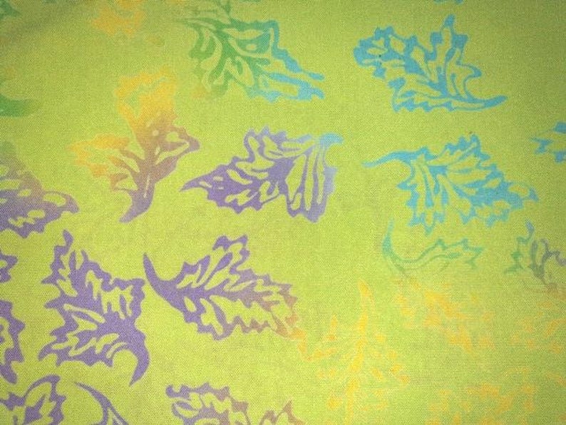 May include: A lime green fabric featuring a repeating pattern of stylized leaves printed in various colors including light blue, purple, and yellow. The leaf shapes are scattered across the surface, creating a vibrant and colorful botanical design.