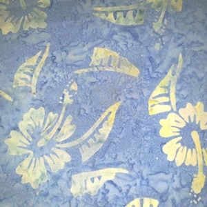 Könnte beinhalten: Blauer Stoff mit einem Muster aus weißen und gelben Hibiskusblüten und Blattformen. Der Stoff hat ein strukturiertes Aussehen mit einem melierten blauen Hintergrund. Das Design erinnert an ein tropisches Thema.
