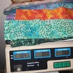 Könnte beinhalten: Ein Stapel verschiedenfarbiger Stoffreste auf einer digitalen Waage. Das Display der Waage zeigt ein Gewicht von 1,04 kg an. Der Stoffstapel besteht aus verschiedenen Mustern und Texturen in den Farben Gelb, Rot, Blau, Orange, Türkis und Grün.