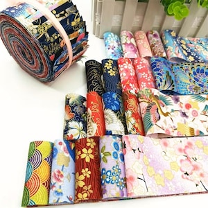 May include: A collection of fabric strips featuring diverse patterns including floral, wave, and crane motifs in vibrant colours like red, blue, gold, and pink. The strips are arranged in a rolled bundle secured with a band and laid out in rows.