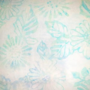 May include: A white fabric featuring a repeating pattern of light blue watercolour-style flowers and leaves. The floral design consists of soft, blurred outlines of daisies and foliage, creating a delicate and airy appearance across the surface.