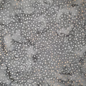 May include: Close-up of a fabric with a mottled grey background and a pattern of white and light beige polka dots. The fabric has a textured appearance, with variations in colour and tone throughout the design. The polka dots vary in size and density.
