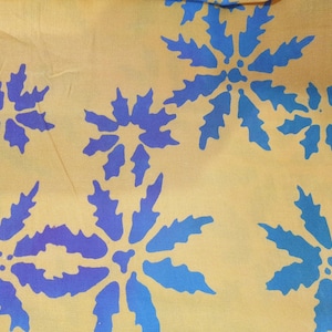 May include: A mustard yellow fabric featuring a repeating pattern of stylized blue floral shapes. The flowers have jagged, leaf-like petals radiating from a central point, creating a bold contrast against the warm, muted yellow background.