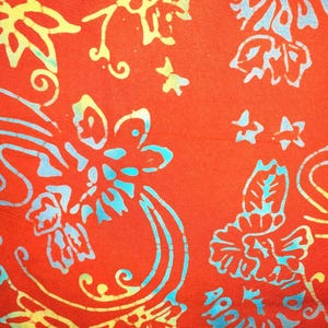 May include: A vibrant orange fabric featuring a repeating batik-style pattern of stylized flowers, leaves, and swirling vines. The design is rendered in shades of bright turquoise and pale yellow, creating a high-contrast, intricate floral motif.