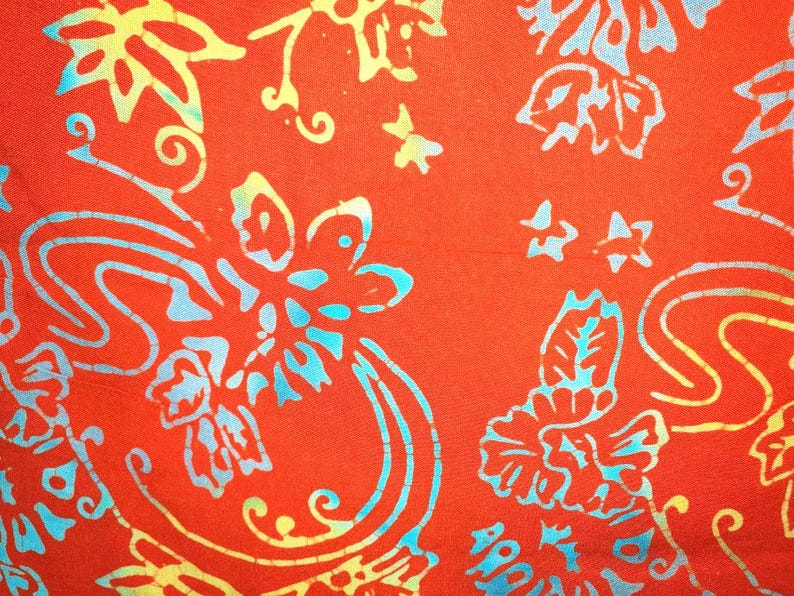 May include: A vibrant orange fabric featuring a repeating batik-style pattern of stylized flowers, leaves, and swirling vines. The design is rendered in shades of bright turquoise and pale yellow, creating a high-contrast, intricate floral motif.