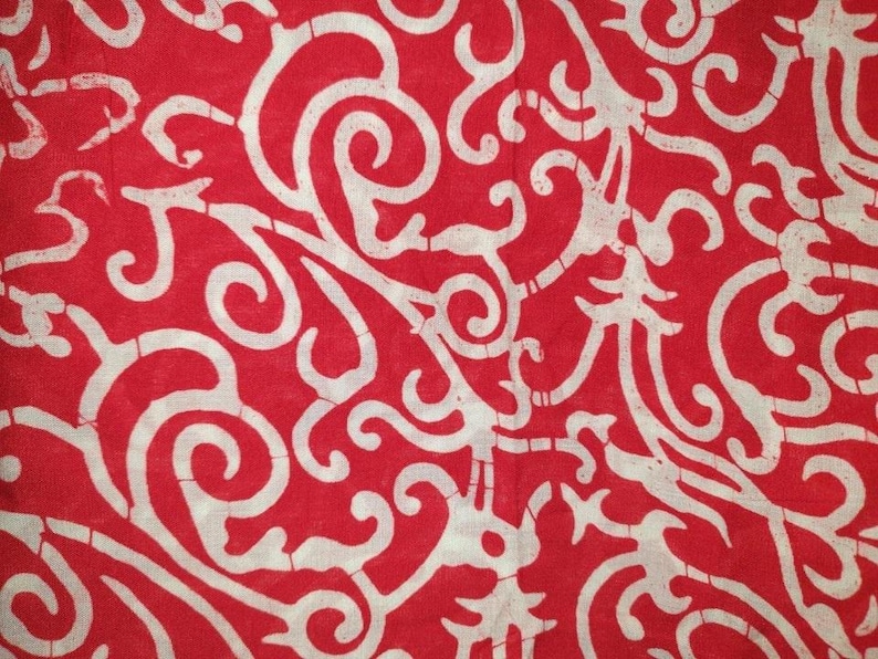 May include: A vibrant red fabric featuring a continuous, repeating off-white pattern of intricate, flowing, and interconnected scrollwork designs. The surface displays a subtle, cracked texture throughout the white lines, characteristic of batik.