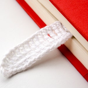 May include: A white crocheted bookmark attached to a red and white book.