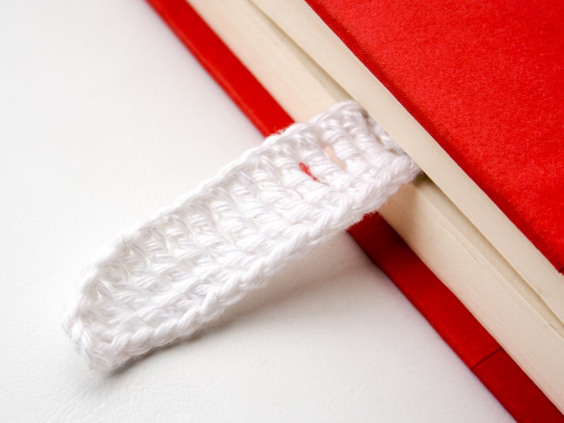 May include: A white crocheted bookmark attached to a red and white book.