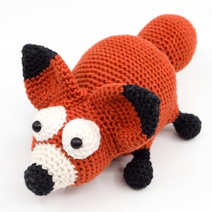 May include: A crocheted fox toy with large white eyes and black pupils. The fox is orange with black ears and feet.