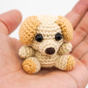 May include: A small crocheted dog toy with brown eyes, a brown nose, and beige and brown fur.