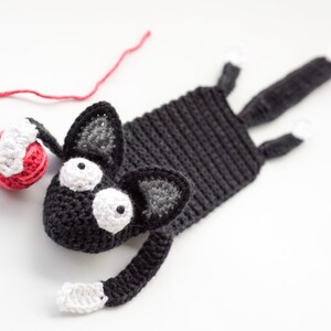 May include: A black crocheted cat bookmark with white yarn accents and large white eyes. The cat is holding a red yarn ball.