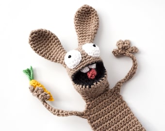 May include: A brown crocheted bunny with large white eyes and a red tongue holds a yellow and green crocheted carrot.
