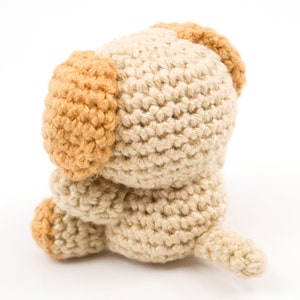May include: A crocheted stuffed dog toy with brown ears and a beige body. The dog is sitting with its head down and its tail curled up.