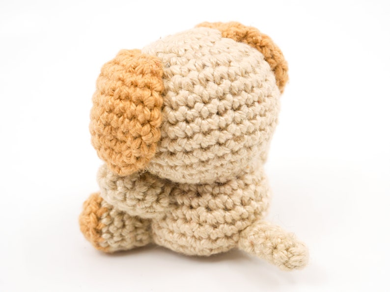 May include: A crocheted stuffed dog toy with brown ears and a beige body. The dog is sitting with its head down and its tail curled up.