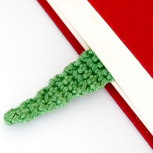 Puede incluir: Un marcap&aacute;ginas de ganchillo verde est&aacute; metido en las p&aacute;ginas de un libro rojo y blanco.