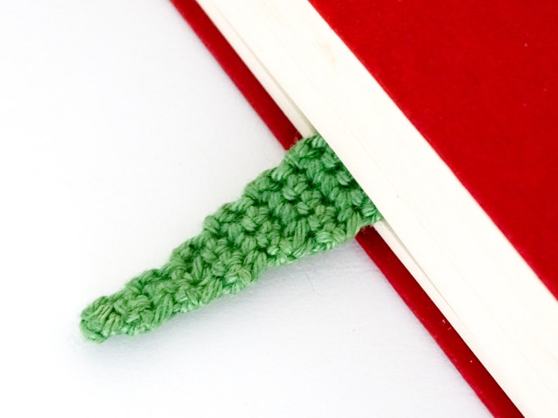 Puede incluir: Un marcap&aacute;ginas de ganchillo verde est&aacute; metido en las p&aacute;ginas de un libro rojo y blanco.