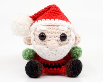 May include: A crocheted Santa Claus ornament with a red hat, white beard, and black eyes. The ornament is sitting on a white surface.