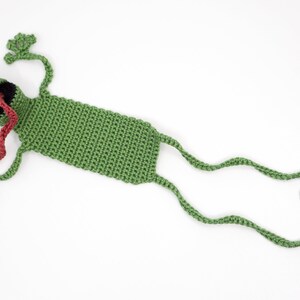 Pu&ograve; includere: Segnalibro a forma di rana verde all'uncinetto con una lunga lingua rossa che sporge. La rana ha occhi bianchi e una bocca nera.