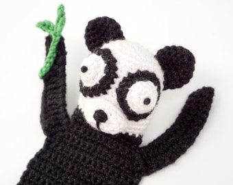 May include: A black and white crocheted panda bear toy holding a green leaf. The panda has large, round eyes and a black nose.