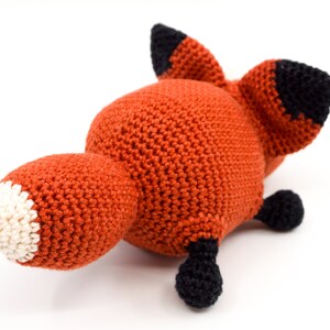 May include: A crocheted fox plush toy with orange fur, black ears and feet, and a white tip on its tail.