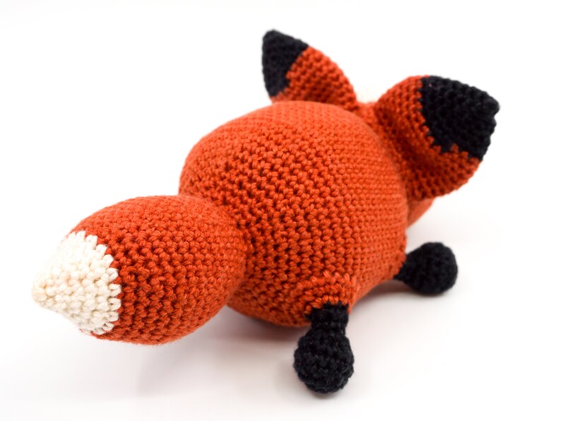 May include: A crocheted fox plush toy with orange fur, black ears and feet, and a white tip on its tail.