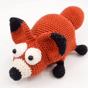 May include: A crocheted fox toy with orange fur, black ears and nose, and large white eyes with black pupils.