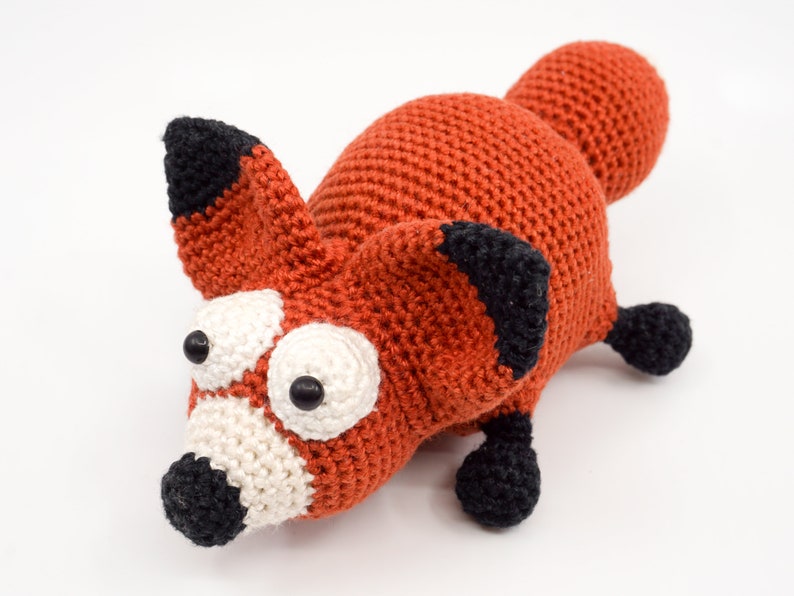 May include: A crocheted fox toy with orange fur, black ears and nose, and large white eyes with black pupils.