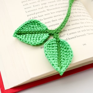 May include: A green crocheted leaf bookmark with two leaves attached to a red string.