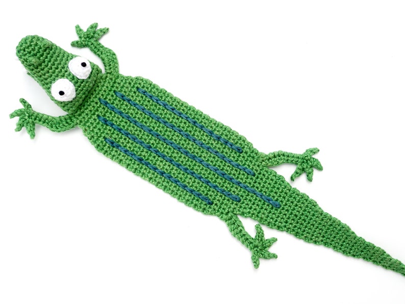 Puede incluir: Marcap&aacute;ginas de cocodrilo verde tejido a crochet con rayas azules y ojos blancos.