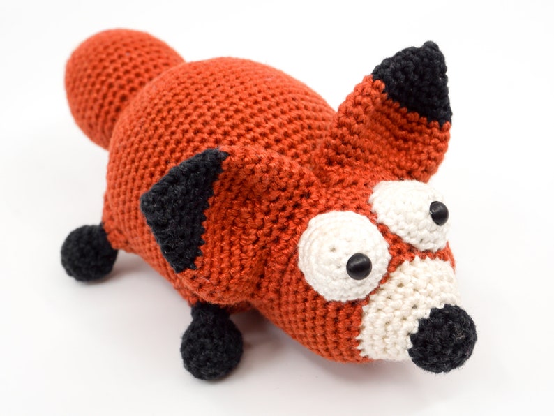 May include: A crocheted fox plush toy with large, white eyes and a black nose. The fox is orange with black ears and feet.