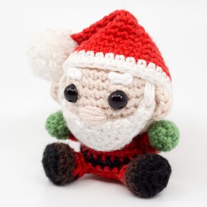 Puede incluir: Un mu&ntilde;eco de Pap&aacute; Noel de crochet con un gorro rojo, barba blanca y ojos negros. El mu&ntilde;eco lleva un traje rojo y blanco con detalles verdes.