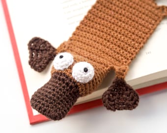 May include: A brown crocheted platypus bookmark with white eyes and a brown snout.