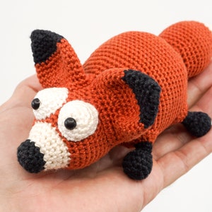 May include: A crocheted fox toy with large white eyes and black accents. The fox is orange and has a white nose and mouth.