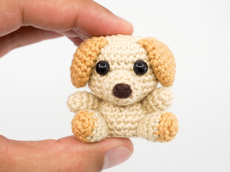 May include: A small crocheted dog toy with brown eyes, a brown nose, and tan ears and paws.