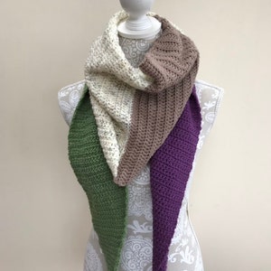 May include: A crocheted scarf in four colors: cream, brown, green, and purple. The scarf is draped over a white mannequin.