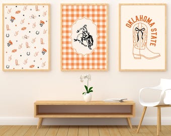 May include: Three framed wall art prints. The left print features a pattern of orange cowboy boots, hats, horseshoes, and OSU logos. The center print shows a black line drawing of a bucking horse on an orange gingham background. The right print displays a cowboy boot with a black bow and the text OKLAHOMA STATE.