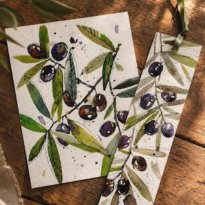 May include: A rectangular card and a vertical bookmark featuring watercolor illustrations of olive branches with dark purple olives and green leaves. The bookmark includes a thin green ribbon attached to the top edge, both on textured paper.