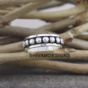 May include: A silver ring featuring a central band decorated with a row of small, raised, polished spheres. The metal has a darkened, oxidized finish in the recessed areas between the beads, creating a high-contrast look. The text SHIVAMDESIGNS is visible.