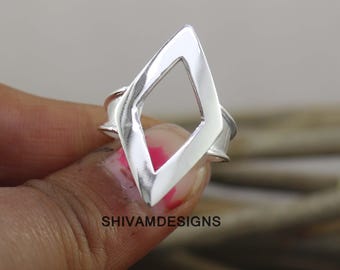 May include: A polished silver ring featuring a prominent, open diamond-shaped centerpiece. The band is smooth and reflective, showcasing a clean, geometric design. The text SHIVAMDESIGNS is printed in black at the base of the ring's central frame.