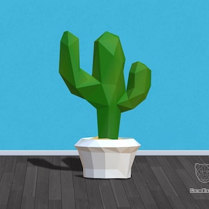 May include: A geometric green cactus in a white polygonal pot. The cactus has multiple arms and is set against a blue wall and dark wood floor. The pot contains a light tan material.