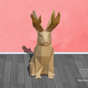 May include: A geometric origami rabbit sculpture made of brown paper. The rabbit is sitting with its ears up and its eyes closed. The sculpture is on a wooden floor in front of a pink wall.