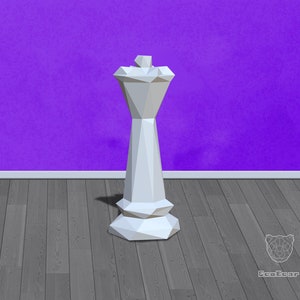 Puede incluir: Una pieza de rey de ajedrez de origami blanca se encuentra en un suelo de madera gris frente a una pared morada.