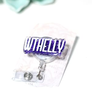 May include: A purple glitter badge reel with the word "WITHELLY" in white lettering. The badge reel has a clear plastic retractable cord and a clear plastic clip.