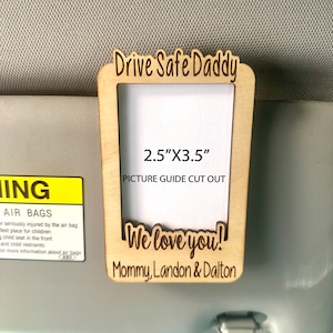 May include: A wooden photo frame with the text "Drive Safe Daddy" and "We love you! Mommy, Landon & Dalton". The frame is designed to be hung on a car visor and has a picture guide cut out that is 2.5 inches by 3.5 inches.