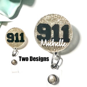 May include: Two gold glitter badge holders with a black 911 and the name Michelle on one. The other has just the 911.