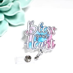 May include: A clear acrylic badge holder with a blue and pink watercolor background. The text "Bless your Heart" is written in black on the badge holder.